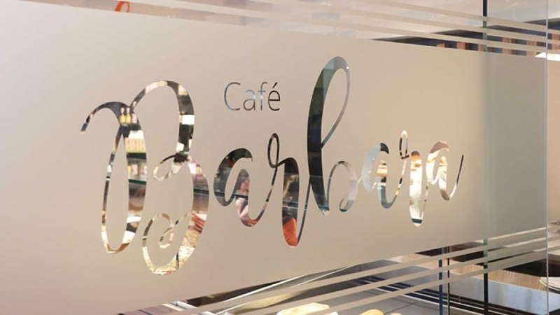 Eine Glaswand mit dem Schriftzug 'Caf&eacute; Barbara' in eleganter Schrift, durch die man in ein Caf&eacute; blicken kann., &copy; Biosph&auml;renhotel Graf Eberhard