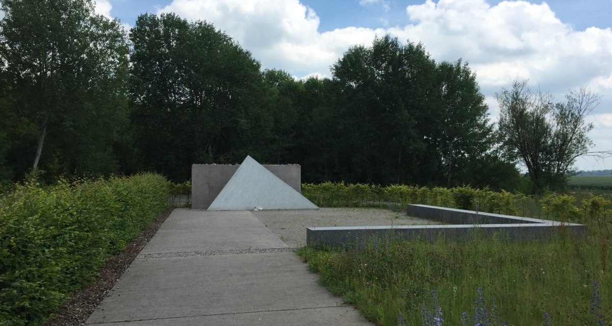 Ein Denkmal mit einer pyramidenf&ouml;rmigen Struktur in einer Gedenkst&auml;tte, umgeben von B&auml;umen und Wiesen unter einem bew&ouml;lkten Himmel., &copy; www.pro-cycl.de