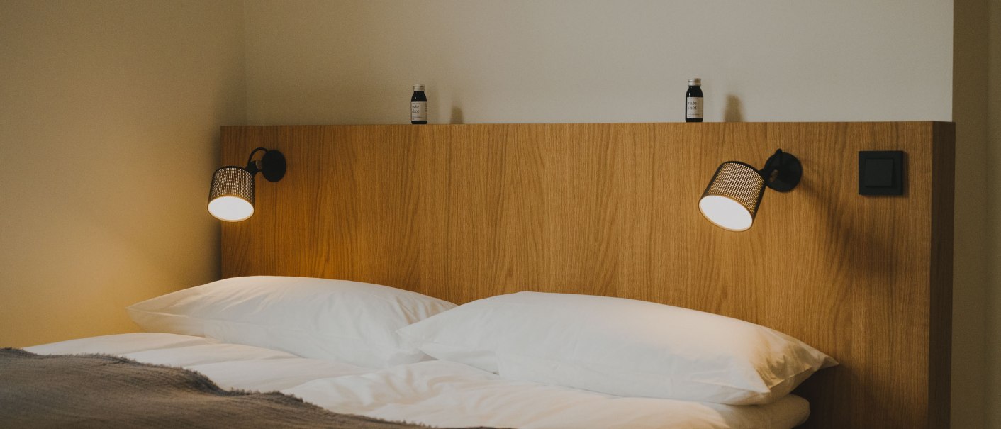 Doppelbett mit Holzrückwand, zwei Leselampen und kleinen Flaschen darauf. Schlichte, moderne Einrichtung., © Peter Oliver Wolff / DAS EDITH