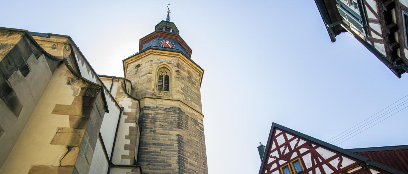 Turm einer Stadtkirche mit Uhr, daneben ein Fachwerkhaus. Der Himmel ist klar und blau., &copy; Stuttgart-Marketing GmbH, Sarah Schmid