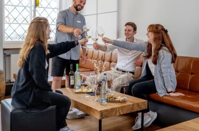 Vier Personen sitzen in einem modernen Raum und stoßen mit Weingläsern an. Auf dem Tisch stehen Weinflaschen und Snacks., © Esslinger Stadtmarketing & Tourismus GmbH Vier Personen sitzen in einem modernen Raum und stoßen mit Weingläsern an. Auf dem Tisch stehen Weinflaschen und Snacks., © Esslinger Stadtmarketing & Tourismus GmbH
