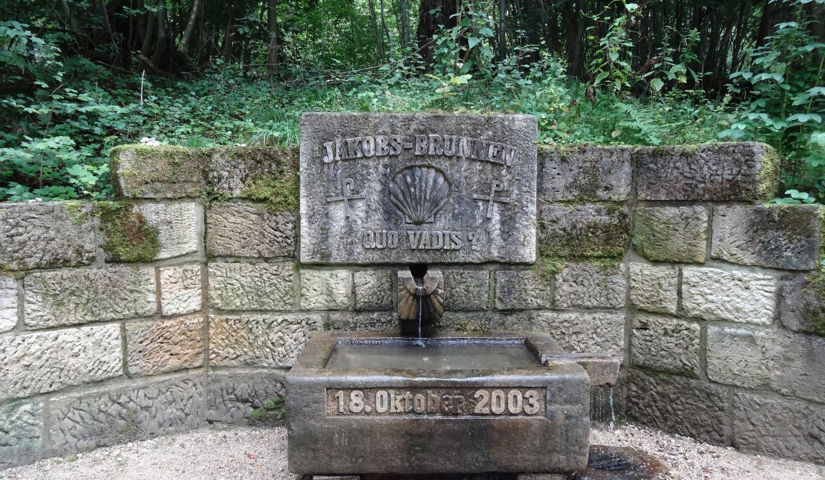 Steinerner Jakobsbrunnen im Wald, mit Inschrift 'Quo Vadis?' und Datum 18. Oktober 2003. Umgeben von grüner Vegetation., © Nürtingen - Stuttgart-Marketing GmbH