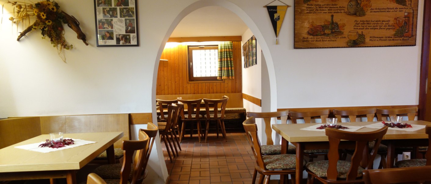 Ein gem&uuml;tliches Restaurant mit Holztischen und -st&uuml;hlen, dekoriert mit Bildern und Blumen. Ein Bogen f&uuml;hrt in einen weiteren Raum., &copy; Besenwirtschaft Familie Nerz