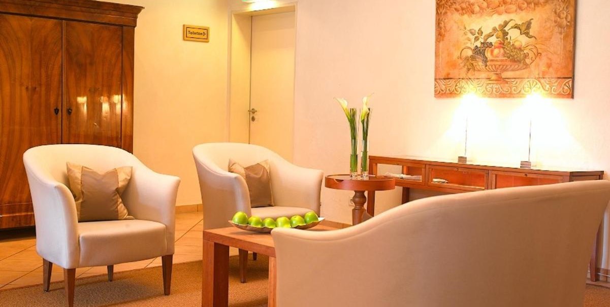 Gem&uuml;tliche Lobby mit wei&szlig;en Sesseln, Holztisch mit gr&uuml;nen &Auml;pfeln, Gem&auml;lde an der Wand und einem Schrank. Dezente Beleuchtung und Pflanzen., &copy; Hotel am Park