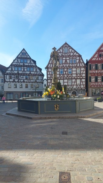 Ein Brunnen mit Osterdekoration steht auf einem gepflasterten Platz, umgeben von traditionellen Fachwerkh&auml;usern unter einem klaren blauen Himmel., &copy; Stadtmarketing