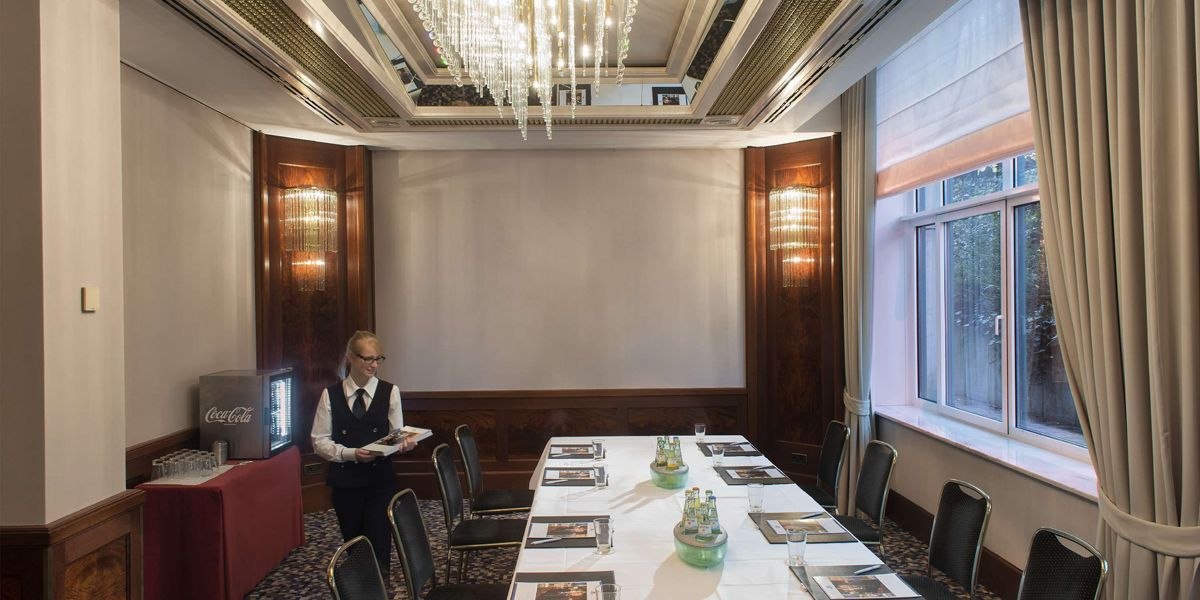 Eleganter Tagungsraum mit Kronleuchter, gedecktem Tisch und Bedienung. Fenster mit Vorhängen, Getränke und Unterlagen auf dem Tisch., © Maritim Hotelgesellschaft mbH