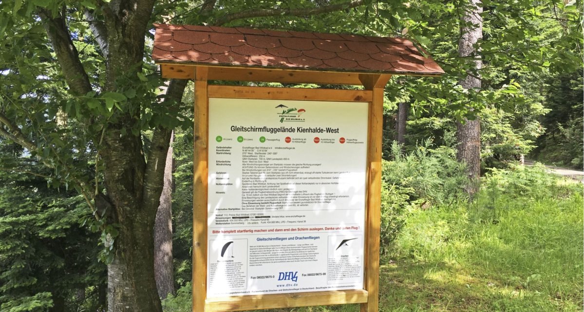 Infotafel im Wald mit Informationen zum Gleitschirmfluggelände Kienhalde-West, umgeben von Bäumen und Gras., © www.pro-cycl.de Infotafel im Wald mit Informationen zum Gleitschirmfluggelände Kienhalde-West, umgeben von Bäumen und Gras., © www.pro-cycl.de