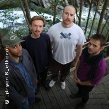 Vier M&auml;nner stehen auf einem Holzsteg im Freien, umgeben von B&auml;umen und einem Fluss im Hintergrund., &copy; links im Bild
