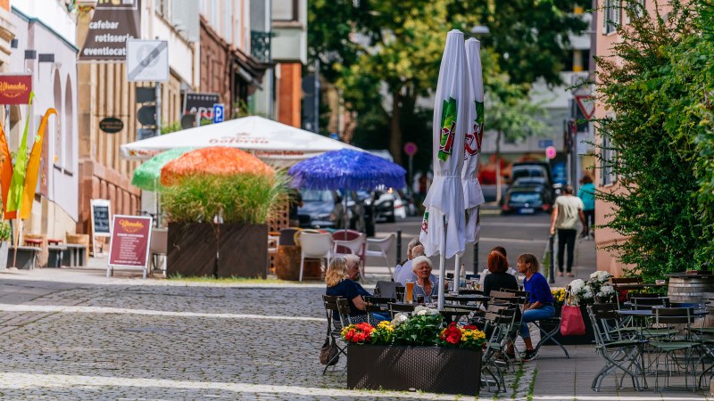 Gem&uuml;tliche Stra&szlig;enszene im Bohnenviertel mit Caf&eacute;s, bunten Sonnenschirmen und Menschen, die im Freien sitzen. Pflastersteine und gr&uuml;ne Pflanzen s&auml;umen den Weg., &copy; SMG Thomas Niederm&uuml;ller