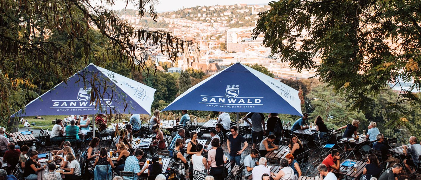 Biergarten auf der Karlshöhe in Stuttgart mit vielen Menschen unter blauen Sonnenschirmen, im Hintergrund die Stadtansicht., © Romeo Felsenreich, sommertage.com Biergarten auf der Karlshöhe in Stuttgart mit vielen Menschen unter blauen Sonnenschirmen, im Hintergrund die Stadtansicht., © Romeo Felsenreich, sommertage.com