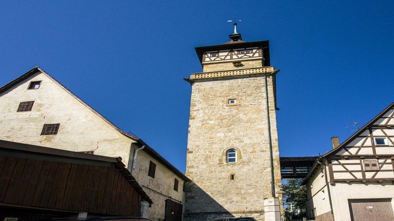 Der Hochwachturm in Waiblingen steht zwischen zwei Fachwerkhäusern unter klarem, blauem Himmel., © SMG, Sarah Schmid