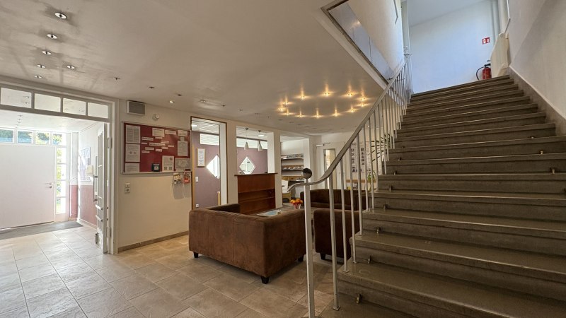 Heller Eingangsbereich mit Treppe, braunen Sofas und Infotafel. Moderne Beleuchtung und Fliesenboden schaffen eine einladende Atmosph&auml;re., &copy; TOMAS