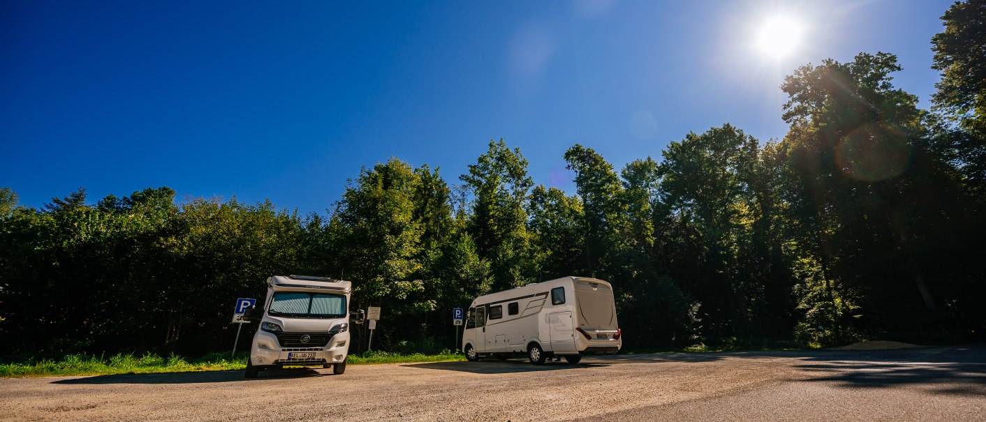 Zwei Wohnmobile stehen auf einem Parkplatz im Stadtpark Welzheim. Der Himmel ist klar und die Sonne scheint hell. B&auml;ume umgeben den Platz., &copy; Stuttgart-Marketing GmbH, Thomas Niederm&uuml;ller
