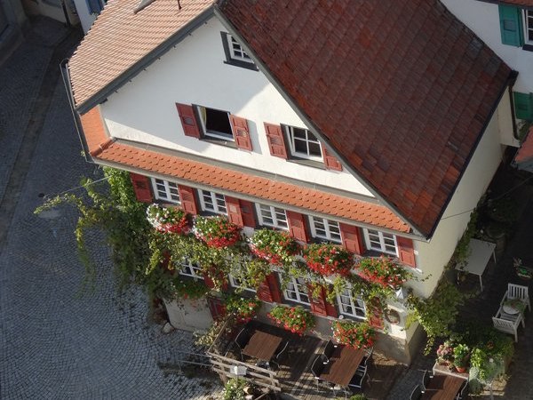 Traditionelles Geb&auml;ude mit roten Fensterl&auml;den und blumengeschm&uuml;ckter Fassade. Im gepflasterten Hof stehen Tische und St&uuml;hle bereit., &copy; Weinstube