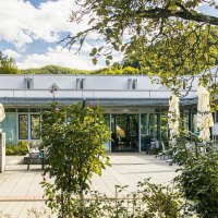 Eingang der Vinzenz Therme in Bad Ditzenbach, umgeben von Bäumen und Pflanzen. Moderne Architektur mit Glasfronten und Skulpturen im Vordergrund., © Stuttgart-Marketing GmbH, Sarah Schmid