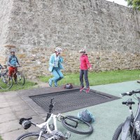 Zwei Personen springen auf einem Trampolin neben Fahrrädern vor einer alten Steinmauer. Weitere Personen stehen mit Fahrrädern daneben., © Schwäbische Alb Tourismusverband e.V.