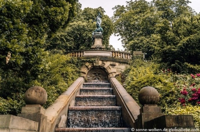 Steintreppe mit Wasserfall, flankiert von Bäumen und Sträuchern, führt zu einer Statue auf einer Balustrade., © Stuttgart Marketing GmbH Steintreppe mit Wasserfall, flankiert von Bäumen und Sträuchern, führt zu einer Statue auf einer Balustrade., © Stuttgart Marketing GmbH