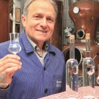 Mann in blauer Jacke h&auml;lt ein Glas mit klarer Fl&uuml;ssigkeit vor einer Destillationsanlage. Auf dem Tisch stehen Flaschen., &copy; Eigenbetrieb Tourismus und Citymanagement Schorndorf