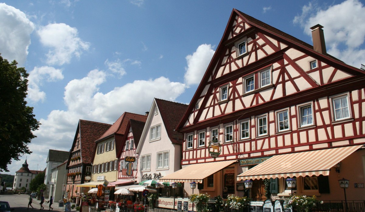 Fachwerkhäuser in Langenburg, Deutschland, mit bunten Fassaden und Geschäften. Im Hintergrund ist ein Schloss zu sehen. Der Himmel ist blau mit Wolken., © Touristikgemeinschaft Hohenlohe, Künzelsau / Marion Schlund Fachwerkhäuser in Langenburg, Deutschland, mit bunten Fassaden und Geschäften. Im Hintergrund ist ein Schloss zu sehen. Der Himmel ist blau mit Wolken., © Touristikgemeinschaft Hohenlohe, Künzelsau / Marion Schlund