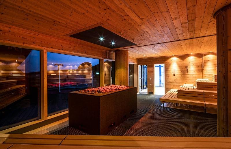 Moderne Sauna mit Holzwänden und -bänken, zentralem Ofen und großen Fenstern. Warmes Licht schafft eine entspannende Atmosphäre., © Mokni's Palais Hotel & Spa Moderne Sauna mit Holzwänden und -bänken, zentralem Ofen und großen Fenstern. Warmes Licht schafft eine entspannende Atmosphäre., © Mokni's Palais Hotel & Spa