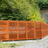 Die Namenswand an der KZ-Gedenkst&auml;tte Leonberg zeigt eingravierte Namen auf rostfarbenem Metall. Sie steht vor einem Tunnel, umgeben von gr&uuml;ner Vegetation., &copy; Stadt Leonberg