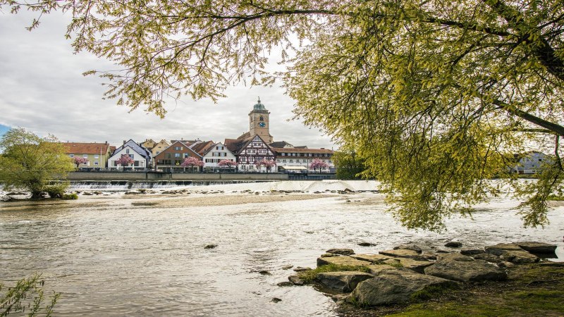 Weitwinkelaufnahme der Fischtreppe in Nürtingen. Im Vordergrund der Fluss mit Steinen, im Hintergrund historische Gebäude und ein Kirchturm, umrahmt von Bäumen., © SMG, Sarah Schmid