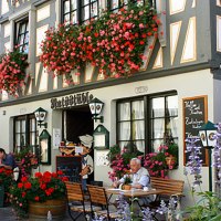 Fachwerkhaus in Besigheim mit Restaurant 'Ratsst&uuml;ble'. Menschen sitzen drau&szlig;en unter Sonnenschirmen, umgeben von bl&uuml;henden Blumen., &copy; Ratsst&uuml;ble Besigheim