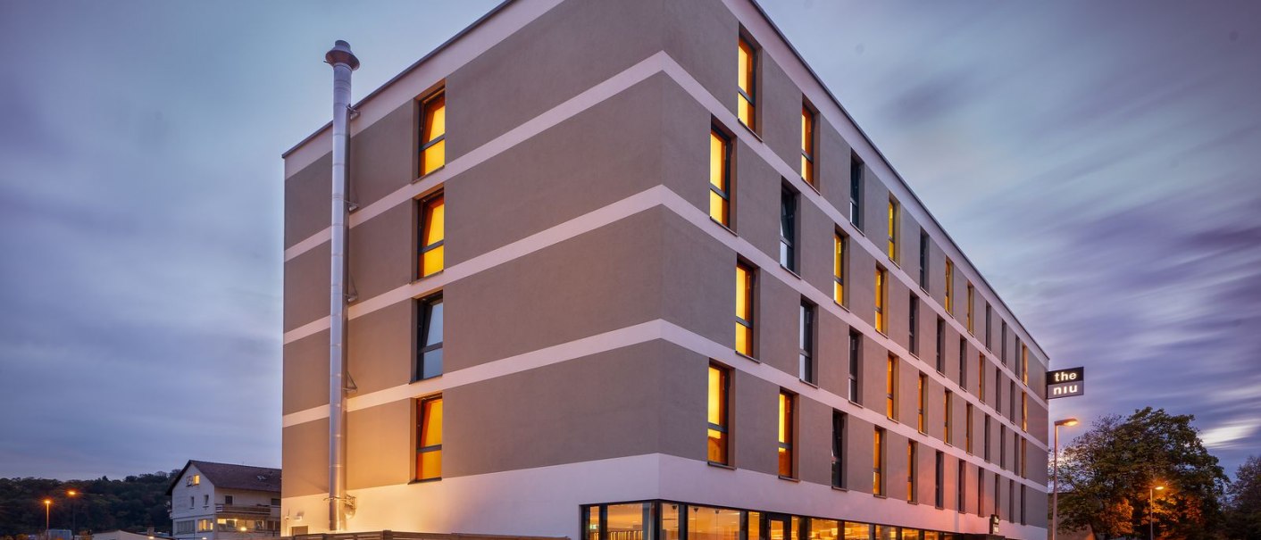 Moderne Hotelaußenfassade bei Dämmerung, beleuchtete Fenster, Schild mit 'the niu'., © Novum Hospitality Moderne Hotelaußenfassade bei Dämmerung, beleuchtete Fenster, Schild mit 'the niu'., © Novum Hospitality