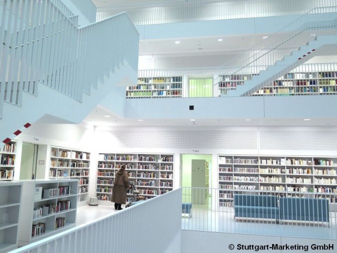 Moderne Innenansicht der Stadtbibliothek Stuttgart mit weißen Wänden, Treppen und Bücherregalen. Eine Person betrachtet Bücher., © Stuttgart Marketing GmbH Moderne Innenansicht der Stadtbibliothek Stuttgart mit weißen Wänden, Treppen und Bücherregalen. Eine Person betrachtet Bücher., © Stuttgart Marketing GmbH