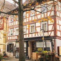 Fachwerkhäuser in der Altstadt von Künzelsau, umgeben von herbstlichen Bäumen. Die Sonne scheint durch die Äste und beleuchtet die Szene., © Stuttgart-Marketing GmbH, Sarah Schmid