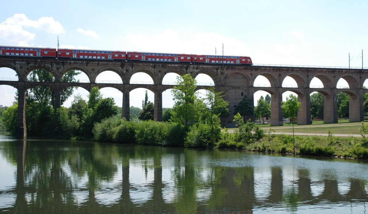 Ein roter Zug fährt über das Enz-Viadukt, das sich über einen Fluss spannt. Der Himmel ist klar, und Bäume säumen das Ufer., © 3B-Tourismus-Team Ein roter Zug fährt über das Enz-Viadukt, das sich über einen Fluss spannt. Der Himmel ist klar, und Bäume säumen das Ufer., © 3B-Tourismus-Team