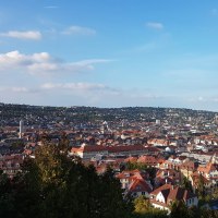 Panoramablick auf eine Stadt mit roten D&auml;chern, umgeben von gr&uuml;nen H&uuml;geln und blauem Himmel., &copy; SMG