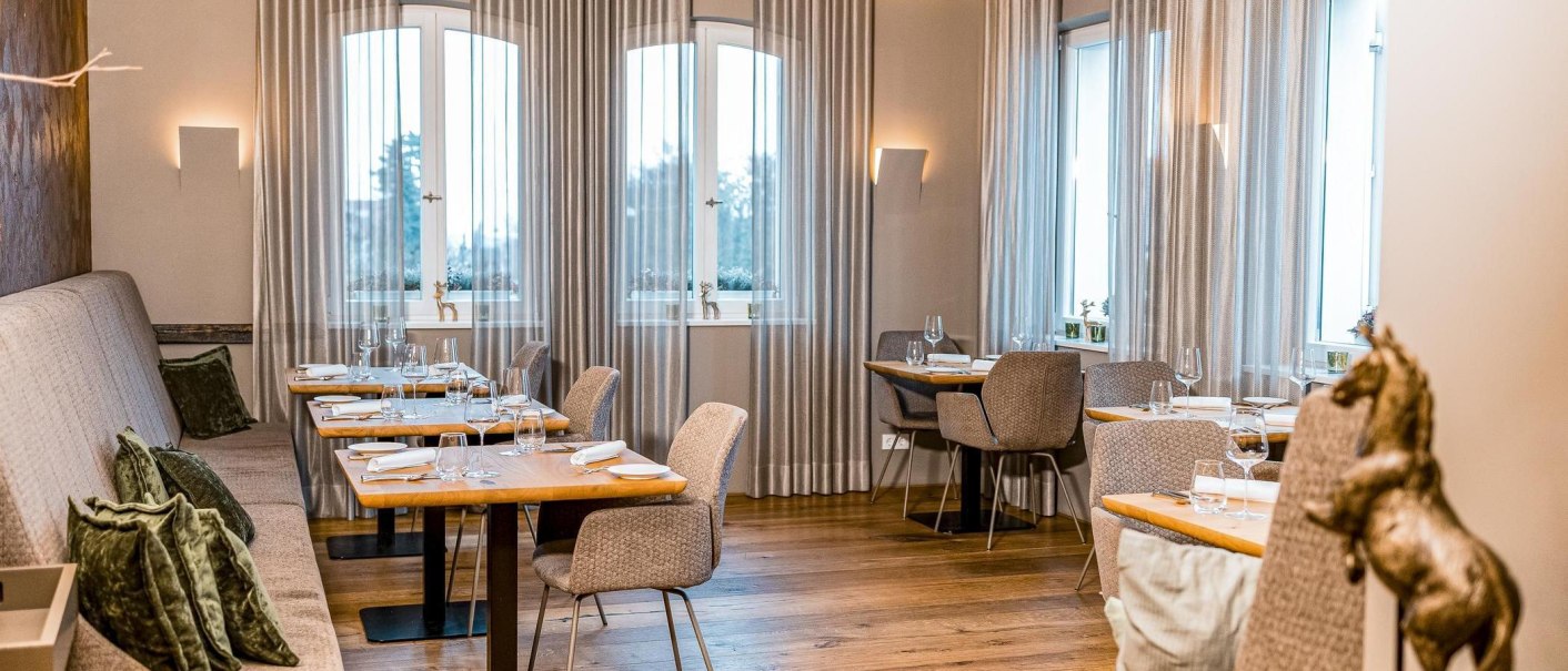 Elegantes Restaurant mit gedeckten Tischen, grauen Vorhängen und Holzboden. Dezente Beleuchtung und stilvolle Dekoration schaffen eine gemütliche Atmosphäre., © New Josch, Stuttgart