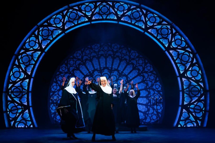 Nonnen tanzen auf der B&uuml;hne des Musicals Sister Act vor einem gro&szlig;en, leuchtenden Kirchenfenster. Die Szene ist lebhaft und farbenfroh., &copy; Ludwigsburg