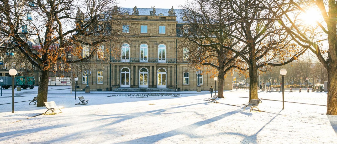Das Neue Schloss im Winter, umgeben von schneebedeckten B&auml;umen und B&auml;nken. Die Sonne scheint durch die &Auml;ste und wirft lange Schatten auf den Boden., &copy; Stuttgart-Marketing GmbH, Sarah Schmid