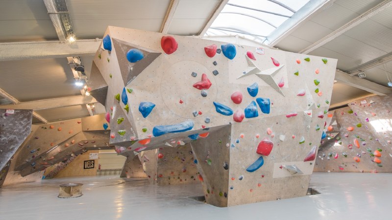 Innenansicht der VELS Boulderhalle mit Kletterw&auml;nden und bunten Griffen unter einem gew&ouml;lbten Dach., &copy; Boulderhalle Vels