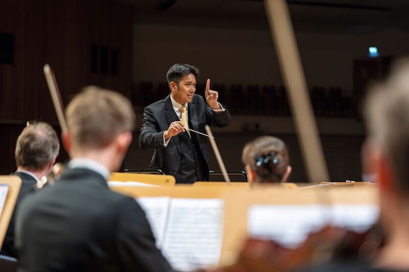 Ein Dirigent führt ein Orchester mit energischen Gesten. Musiker im Vordergrund konzentrieren sich auf ihre Noten., © Rotary-Hilfe e.V., Leonberg-Weil der Stadt Ein Dirigent führt ein Orchester mit energischen Gesten. Musiker im Vordergrund konzentrieren sich auf ihre Noten., © Rotary-Hilfe e.V., Leonberg-Weil der Stadt