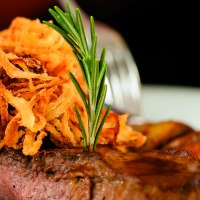 Zwiebelrostbraten mit knusprigen Zwiebeln und Rosmarin garniert. Im Hintergrund sind Beilagen zu sehen., © Kzenon-Fotolia
