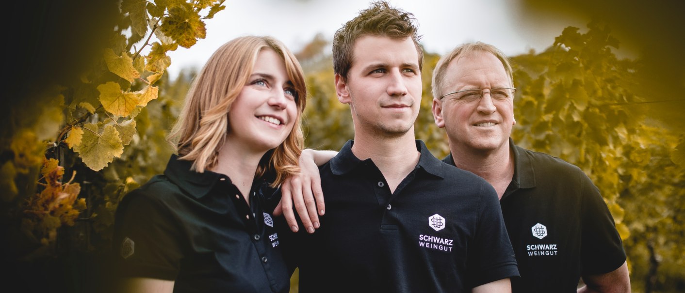 Drei Personen in schwarzer Kleidung mit dem Logo "Schwarz Weingut" stehen lächelnd in einem Weinberg. Sie wirken zufrieden und verbunden., © Weingut Schwarz Drei Personen in schwarzer Kleidung mit dem Logo "Schwarz Weingut" stehen lächelnd in einem Weinberg. Sie wirken zufrieden und verbunden., © Weingut Schwarz