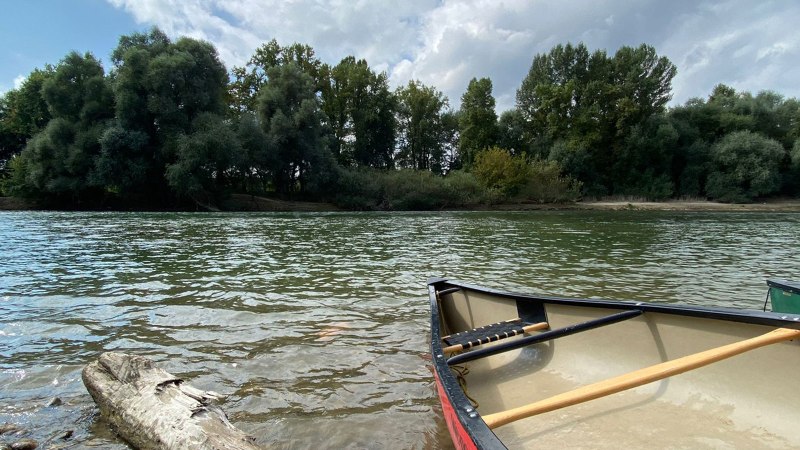 Ein Kanu liegt am Ufer eines ruhigen Flusses, umgeben von dichtem Wald und bewölktem Himmel., © Manuel Mattern Ein Kanu liegt am Ufer eines ruhigen Flusses, umgeben von dichtem Wald und bewölktem Himmel., © Manuel Mattern