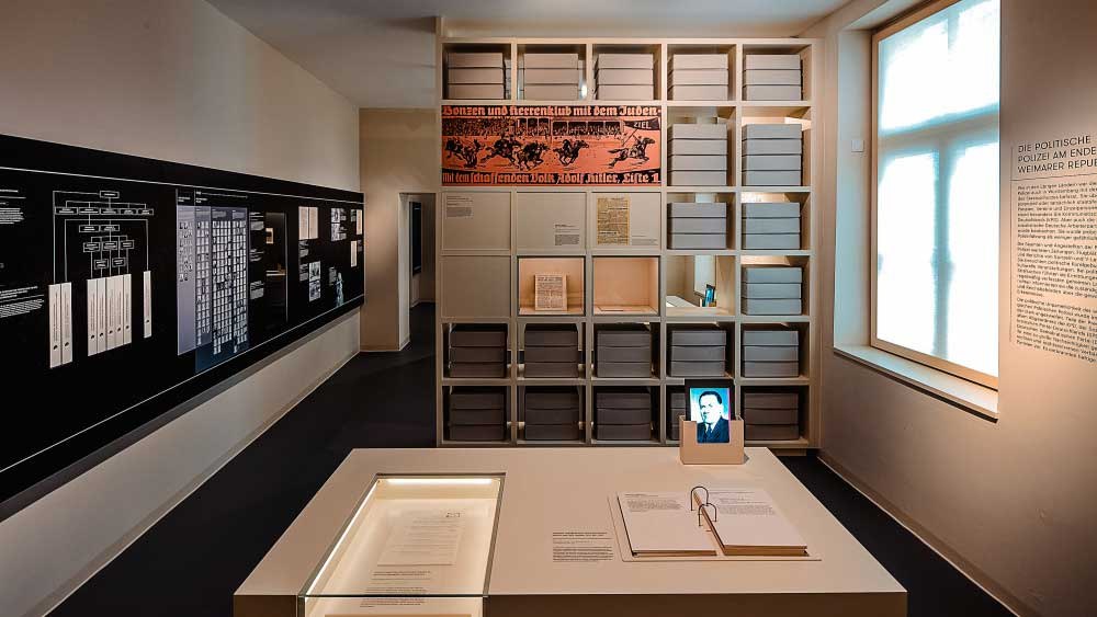 Ein Ausstellungsraum mit Regalen voller Archivboxen, Dokumenten auf einem Tisch und Informationstafeln an den Wänden., © Haus der Geschichte Baden-Württemberg