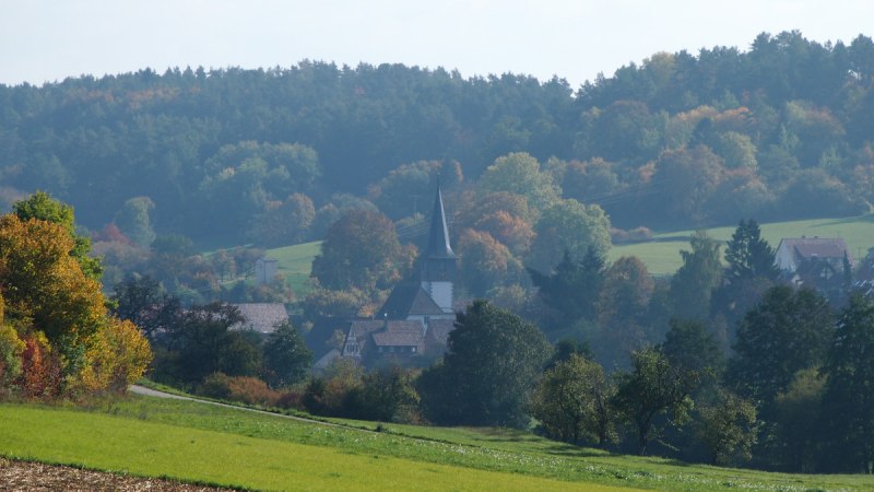 Blick auf ein Dorf mit Kirchturm, umgeben von grünen Feldern und herbstlichen Wäldern unter blauem Himmel., © Natur.Nah. Schönbuch & Heckengäu Blick auf ein Dorf mit Kirchturm, umgeben von grünen Feldern und herbstlichen Wäldern unter blauem Himmel., © Natur.Nah. Schönbuch & Heckengäu