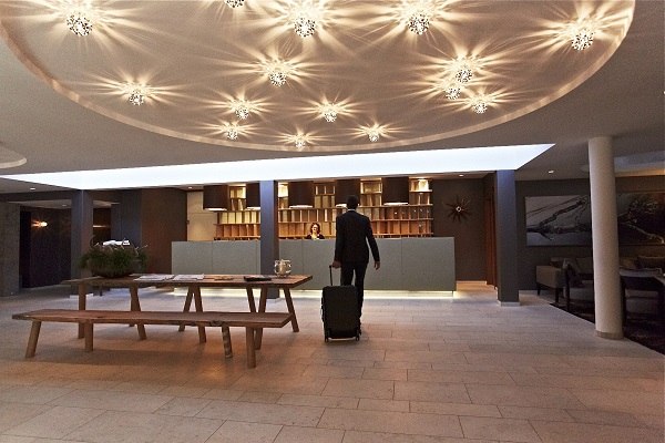 Ein Mann mit Koffer steht an der Rezeption des Waldhotels Stuttgart. Die Decke ist mit stilvollen Leuchten dekoriert., © Waldhotel Stuttgart GmbH Ein Mann mit Koffer steht an der Rezeption des Waldhotels Stuttgart. Die Decke ist mit stilvollen Leuchten dekoriert., © Waldhotel Stuttgart GmbH
