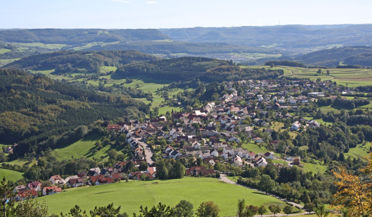 Luftaufnahme eines Dorfes inmitten einer grünen, hügeligen Landschaft mit Wäldern und Feldern unter blauem Himmel., © Foto: Frieder Kopper Luftaufnahme eines Dorfes inmitten einer grünen, hügeligen Landschaft mit Wäldern und Feldern unter blauem Himmel., © Foto: Frieder Kopper