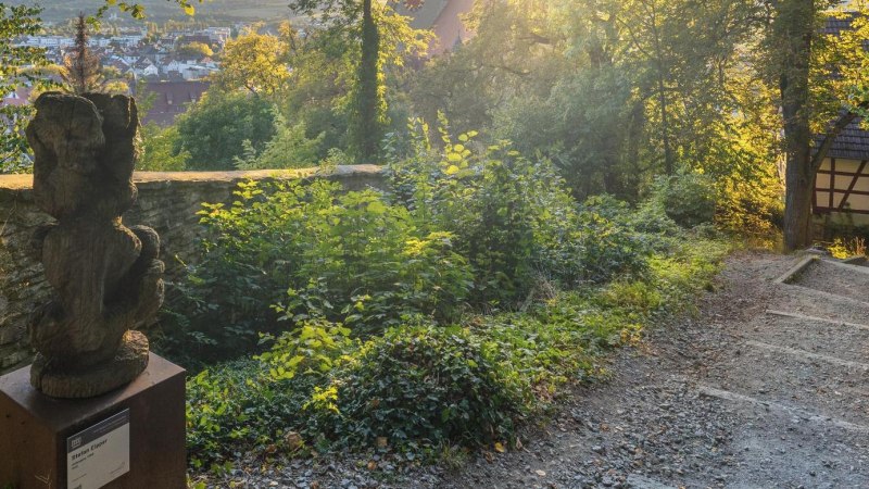 Skulpturenpfad in Herrenberg mit einer Holzskulptur, umgeben von B&auml;umen und einem Fachwerkhaus im Hintergrund. Die Abendsonne beleuchtet die Szene., &copy; Stuttgart-Marketing GmbH, Martina Denker