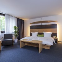Modernes Hotelzimmer mit Doppelbett, Sessel, Tisch, Laptop und Glas Wein. Fenster mit Vorhängen, Pflanze und stilvolle Beleuchtung., © Hotel Berlin aZIS Hotel BetriebsGmbH