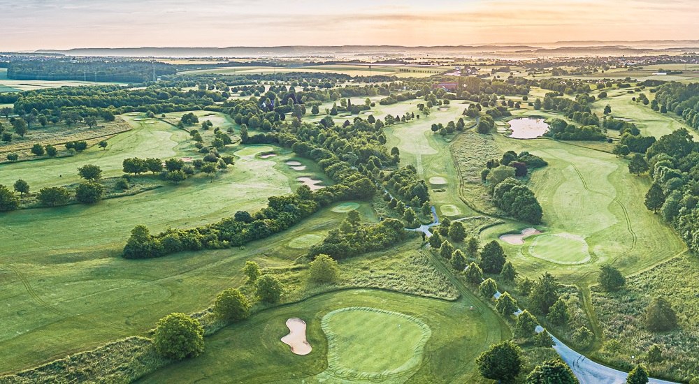 Luftaufnahme des Golfclubs Domäne Niederreutin mit gepflegten Fairways, Bunkern und Clubhaus im Hintergrund bei Sonnenuntergang., © Golfclub Domäne Niederreutin