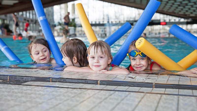 Vier Kinder im Schwimmbad lehnen am Beckenrand und halten bunte Schwimmnudeln. Sie l&auml;cheln und tragen Badeanz&uuml;ge., &copy; Badezentrum Sindelfingen