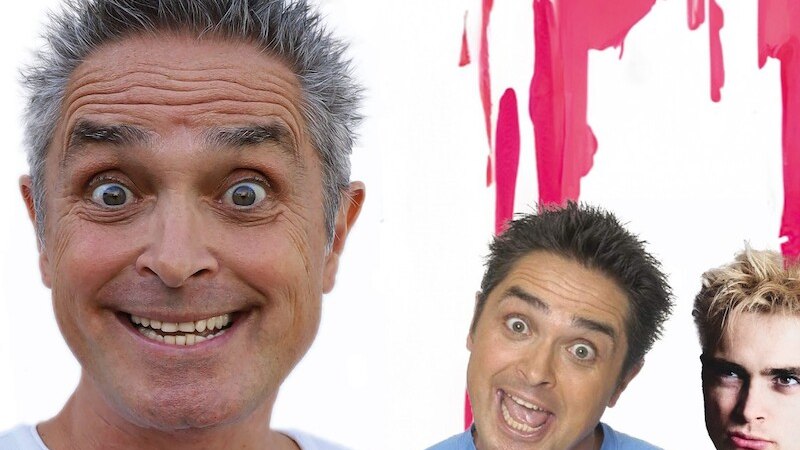 Ein Mann mit grauen Haaren lächelt in die Kamera. Im Hintergrund sind zwei weitere Männer vor einem pinken Hintergrund zu sehen., © Mauerwerk GmbH Ein Mann mit grauen Haaren lächelt in die Kamera. Im Hintergrund sind zwei weitere Männer vor einem pinken Hintergrund zu sehen., © Mauerwerk GmbH