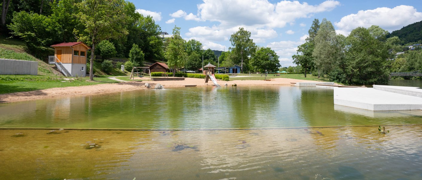 Das Kocherfreibad in K&uuml;nzelsau zeigt einen Sandstrand, einen Spielplatz mit Rutsche und Schaukeln, umgeben von B&auml;umen und einem klaren Himmel., &copy; Olivier Schniepp, Foto Linke GmbH